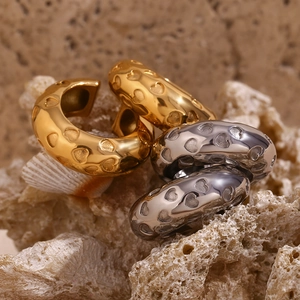 Detail of gold and silver C-shaped hoop earrings with embossed heart patterns on coral