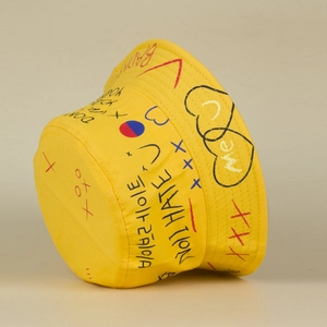 Detailed side profile of a yellow bucket hat featuring artistic graffiti print and hearts