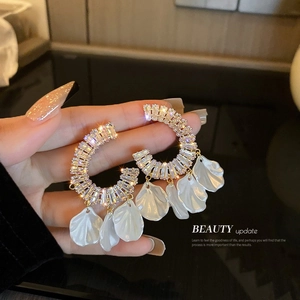 Détail de boucles d'oreilles créoles dorées avec cristaux et pétales de fleurs blanches