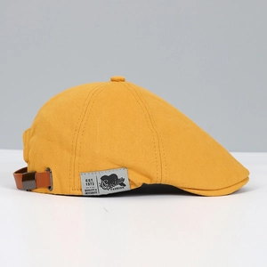 Detail of yellow canvas beret featuring side brand logo and leather adjustable strap
