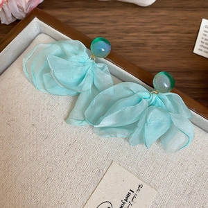 Close-up of light cyan fabric flower earrings with teal resin studs on a texture tray