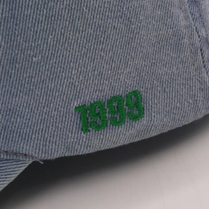 Macro shot of green 1999 embroidery on washed light blue denim baseball cap detail