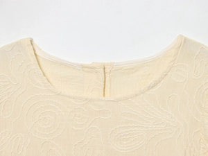 Détail du haut en coton beige avec broderie ondulée blanche délicate sur l'encolure