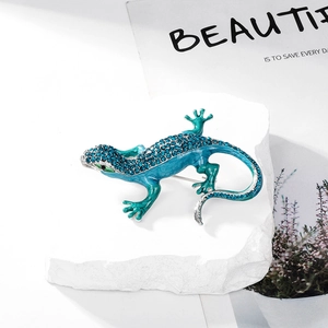Macro shot of lizard brooch with blue-green enamel and crystals on white textured stone