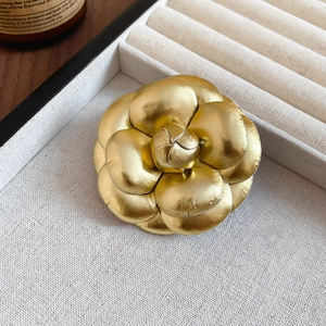 Macro shot of 3D golden leather camellia flower brooch on a textured beige box