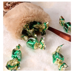 Close-up of brown plush Christmas stocking filled with green wrapped candies on white snow