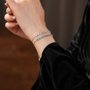 Detail of silver clover bracelets with emerald and white zircon stones on model's wrist