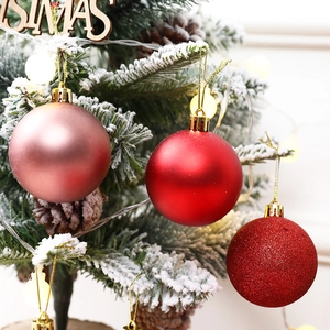 Red and pink Christmas tree ornaments with matte and glitter finish hanging on snowy branches