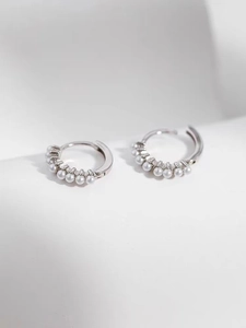 Détail des boucles d'oreilles créoles en perles argentées au fini poli sur fond blanc pur