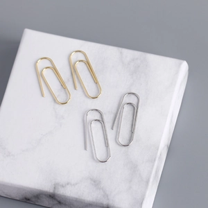 Macro detail of gold and silver safety pin earrings on a marble display surface