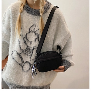 Détail du sac bandoulière en nylon noir avec breloque tendance sur un sweat à capuche