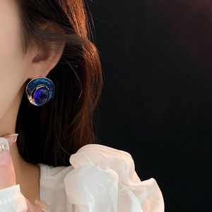 Close-up of vintage gold and blue enamel oval stud earring with inset gemstone on ear