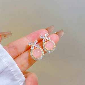 Close-up of golden bow earrings featuring pink round gemstones and shimmering crystals