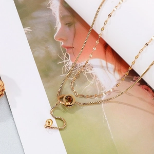 Detail view of gold double layer necklace with intertwined rings and ball pendant