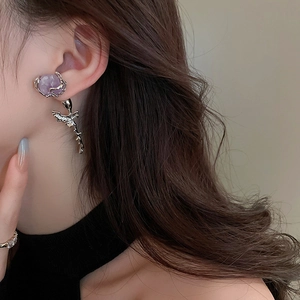 Detail of silver rose earrings with purple crystals worn by a model in soft lighting