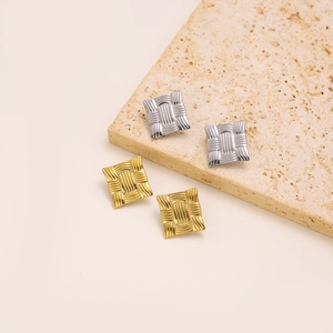 Detail of square woven texture earrings in gold and silver finish on a stone base