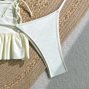 Detailed top view of cream bikini top with ruffle edges and ties on woven mat background