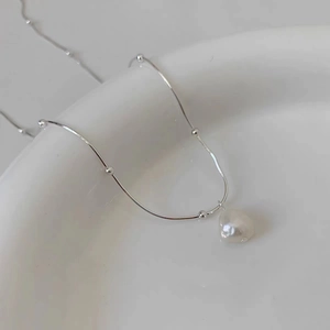 Baroque pearl pendant on silver snake chain necklace placed on white ceramic plate