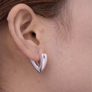 Close-up of heart-shaped silver earrings worn to show scale and polished metallic finish