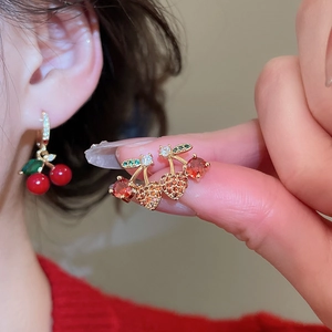 Macro detail of cherry stud earrings with red and green cubic zirconia in gold plating