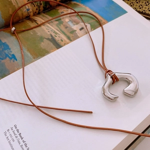 Detail view of silver U-shaped metal pendant necklace on brown leather cord