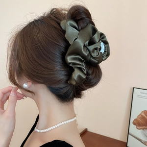 Macro detail of elegant dark green pleated satin fabric texture on a large hair claw clip