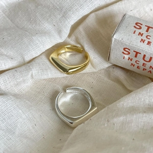Minimalist silver and gold adjustable open rings shown on a textured linen fabric background