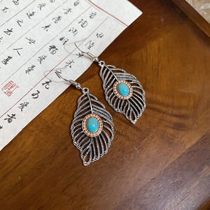Detail of bohemian leaf-shaped earrings with oval turquoise inlay on vintage wood