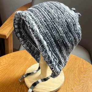 Close-up of winter knitted beanie with earflaps and straps in grey mixed yarn