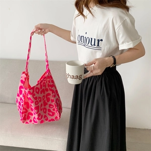 Side view of a large pink leopard print canvas tote bag held by a model in a cozy setting