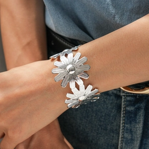 Gros plan d'un bracelet manchette fleur argentée avec détails de marguerites au poignet