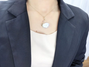 Détail d'un pendentif cygne doré avec perle baroque sur un mannequin féminin