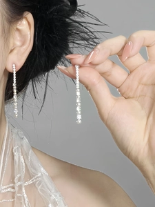 Close-up of long linear silver earrings with sparkling crystals and pearl tassels on model