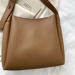 Close-up of caramel matte leather tote bag styled with a minimalist art book on white fabric