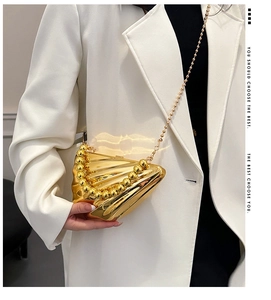 Dettaglio di borsa da sera dorata a conchiglia con manico di perle su blazer bianco