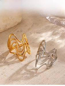 Detail of irregular wave layered rings in gold and silver finishes on stone background