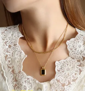 Close-up of double-layer gold chain necklace with a black rectangular pendant on a neck