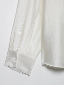 Detailed macro view of ivory satin shirt cuff showing high-end silky texture and button