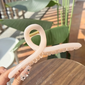 Detail of pink resin hair claw clip with golden spring held in hand outdoors