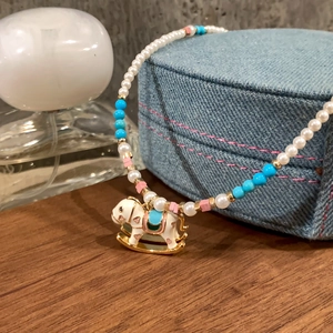 Detail of beaded pearl necklace featuring a rocking horse pendant on wood texture