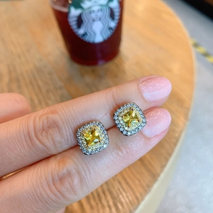 Macro detail of square halo stud earrings with yellow cushion-cut stone on a finger