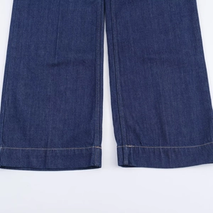 Détail d'un jean en denim bleu foncé avec ourlet large à double piqûre et coutures dorées