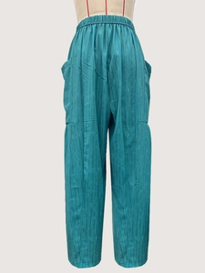 Detailed view of elastic high waist and vertical stripes on turquoise pleated trousers