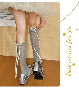 Detail of grey balletcore leg warmers with white ribbon bows and sequined shoes