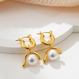 Close-up of golden pearl earrings with detachable U-shaped design on a white pedestal