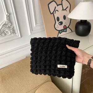 Detail of black cloud puff makeup bag with Sozakka tag held by a hand in a room