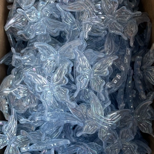Close-up of bulk transparent blue iridescent acrylic butterfly pendants for DIY crafts