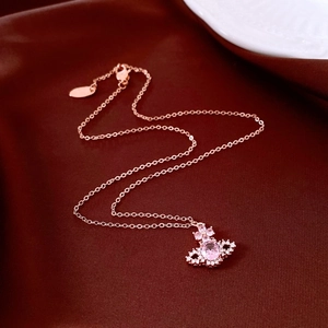 Detailed close-up of rose gold planet-shaped pendant with pink stone on red silk background