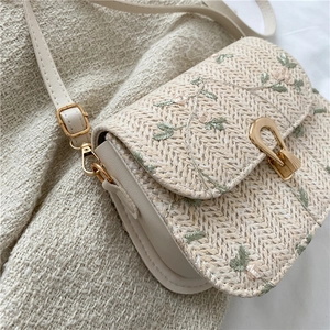 Beige straw woven saddle bag with floral embroidery and adjustable leather strap