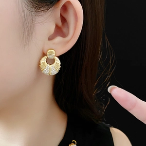 Détail de créoles dorées avec zircons portées par un mannequin sur fond noir élégant et chic